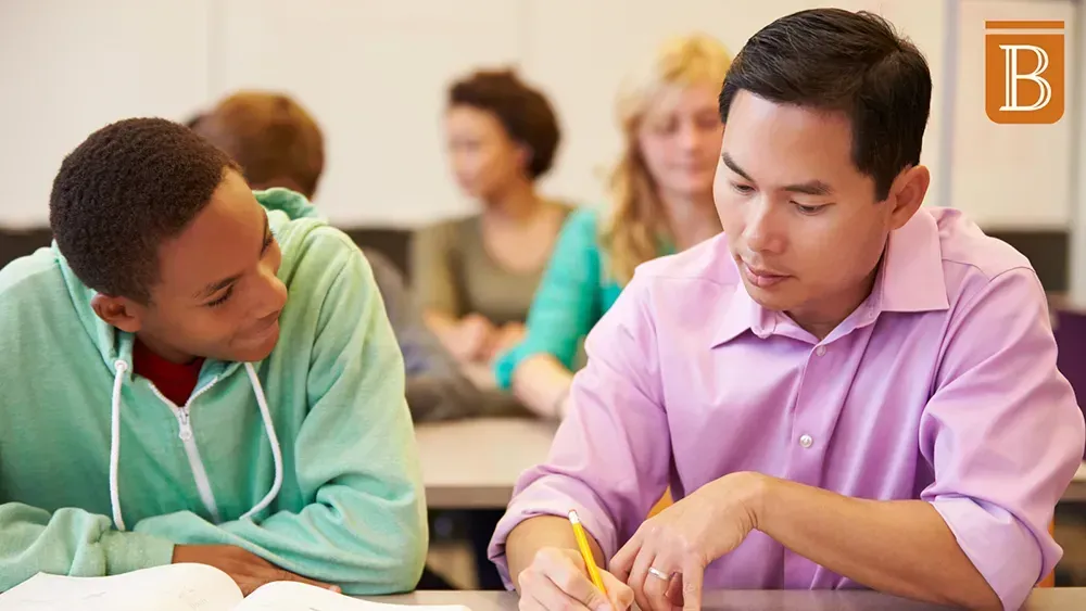 high school student and teacher working at a desk