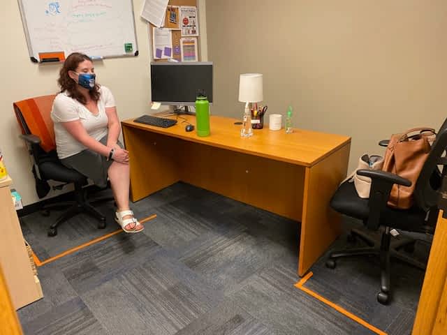 A woman wearing a mask is sitting at a desk in an office.