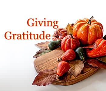 A wooden cutting board topped with pumpkins and leaves.