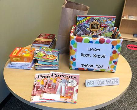 A table with a box of books and a sign that says umom book drive thank you