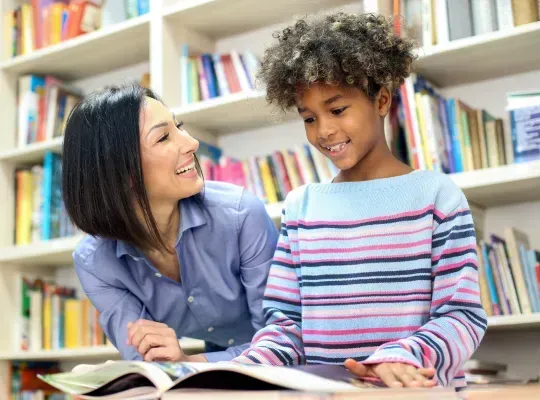 student looking at a book, adult looking up at child