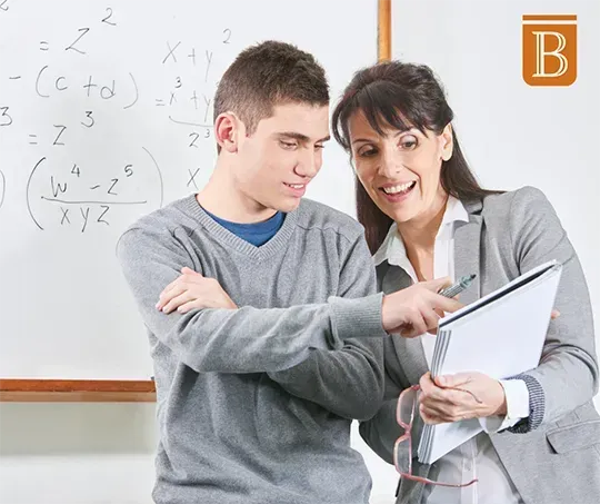 high school aged boy and teacher looking at a notebook while standing