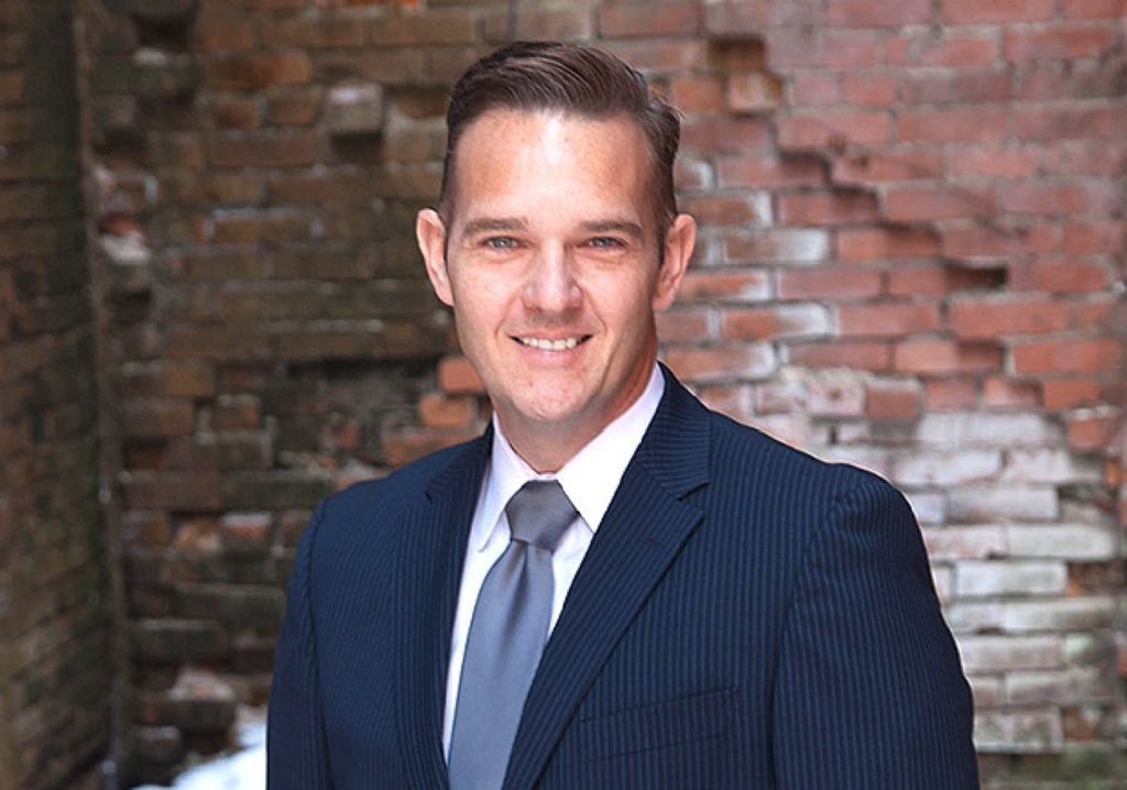 A man in a suit and tie is standing in front of a brick wall.