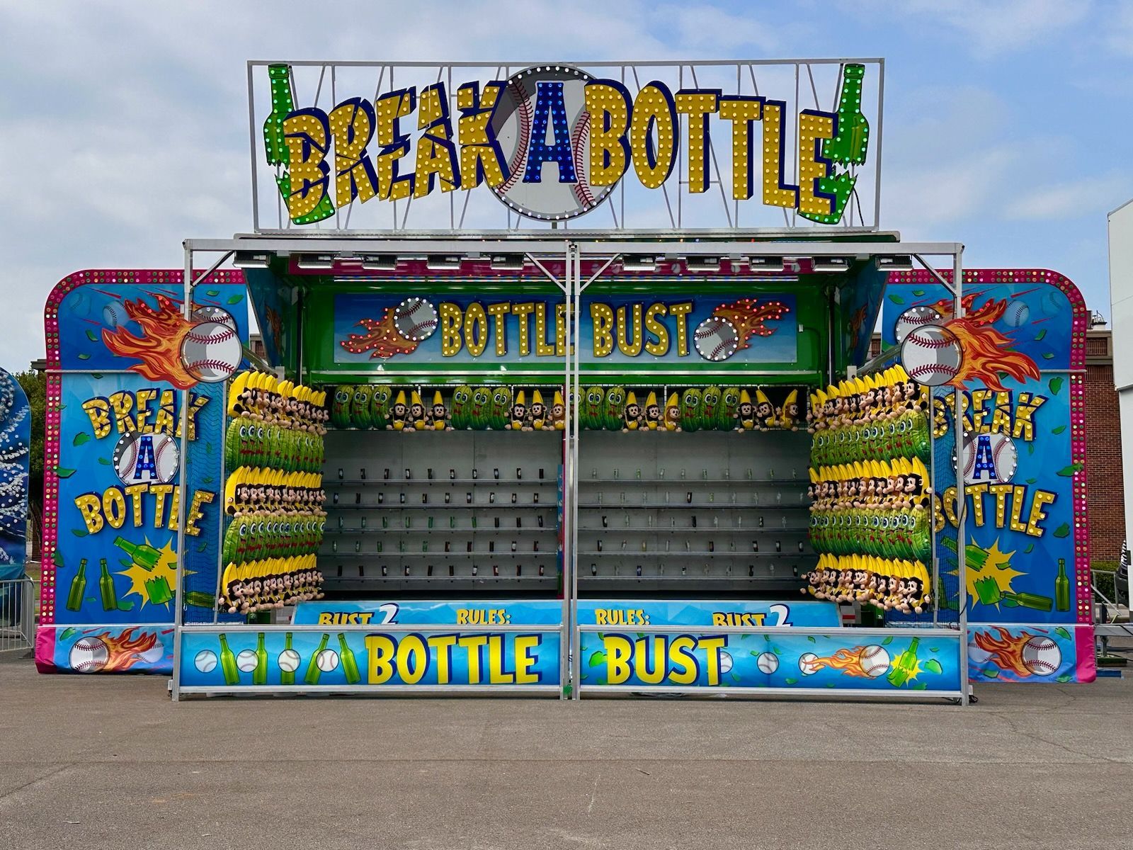 Food vendor booths at an outdoor fair, flags overhead, signs for funnel cakes, pizza, and drinks.