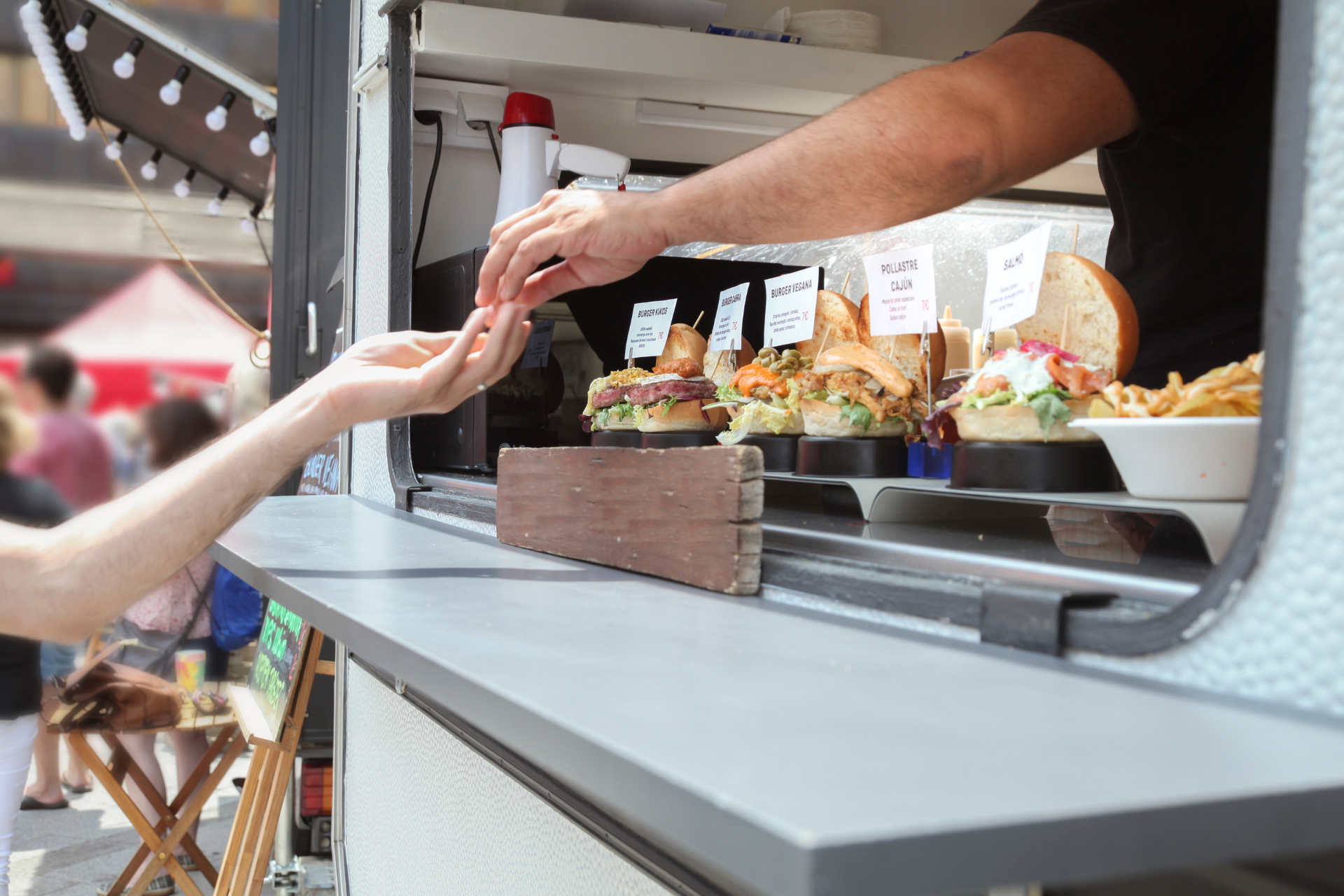 Person paying for food at a food truck window; burgers and fries visible.
