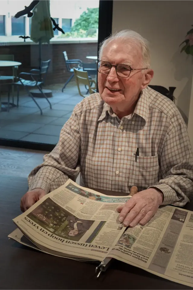 Een vrouw in een blauwe operatiekleding lacht naast een oudere man in een geruit overhemd.