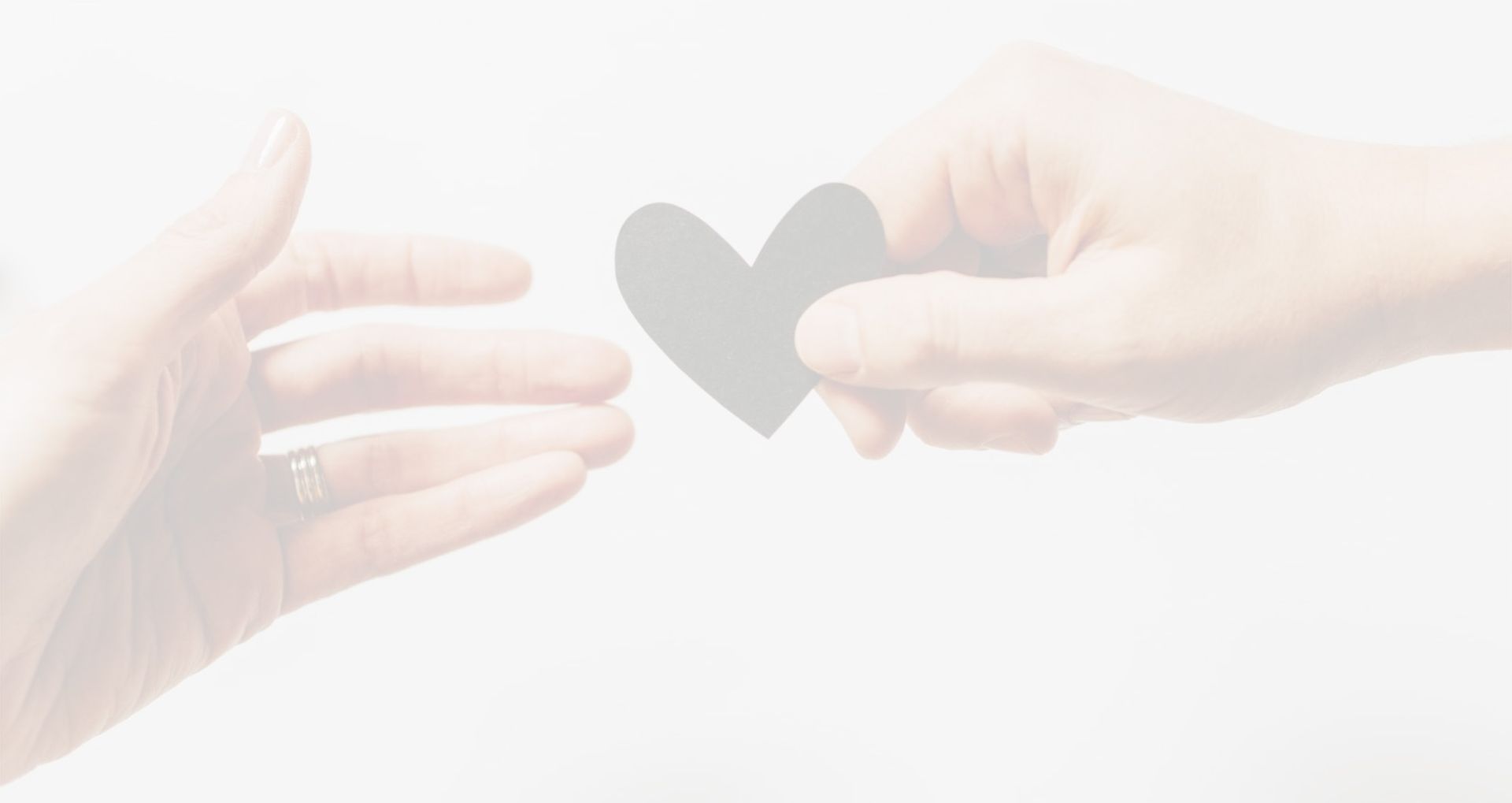 Twee handen, waarvan de ene een grijs hart vasthoudt, reiken naar de andere. Witte achtergrond.