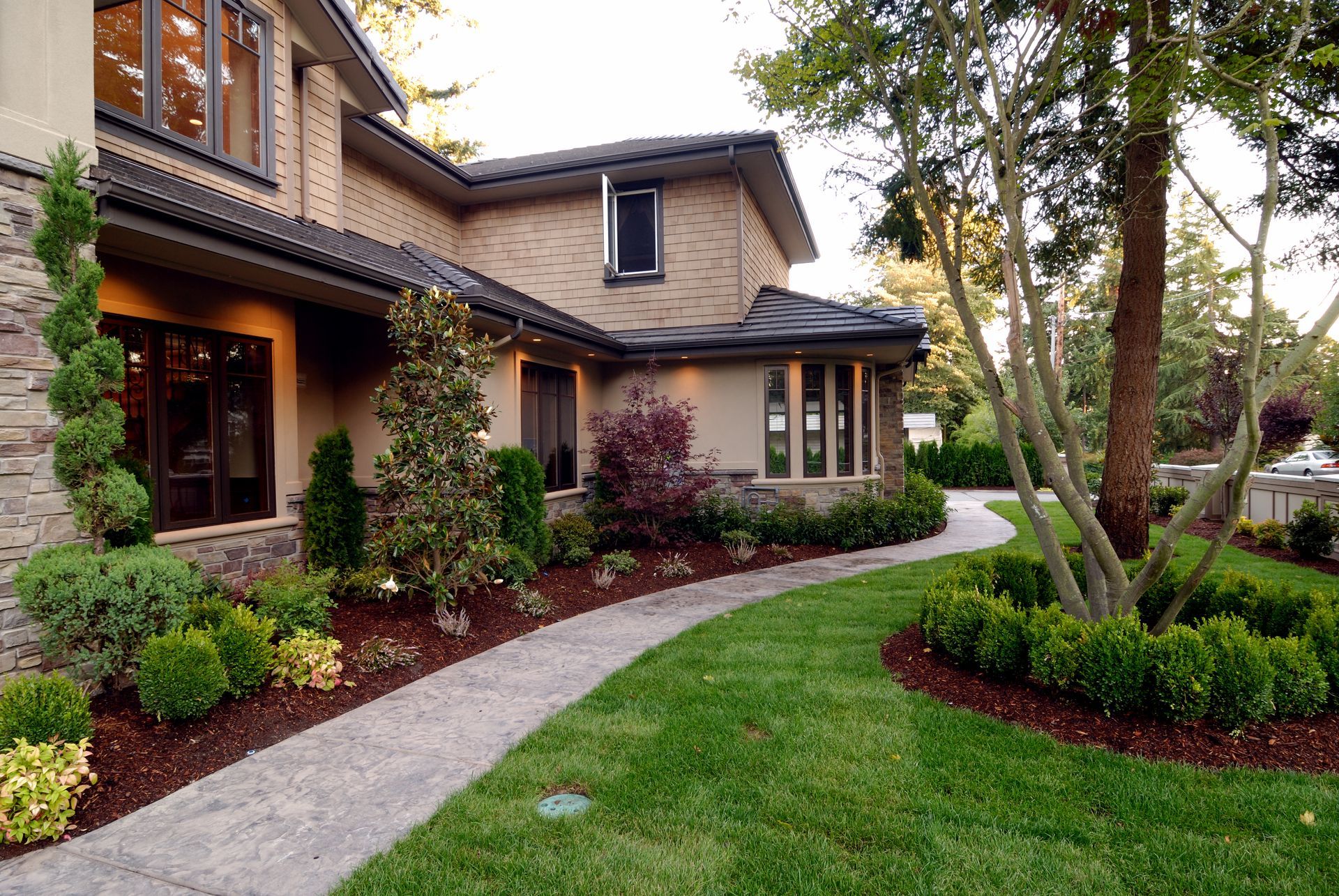 A lush green yard with trees , bushes , and mulch.