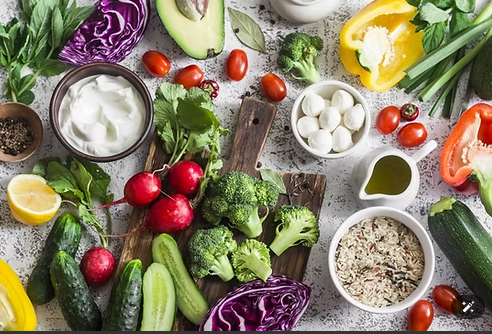 Vegetables and other ingredients arranged on a white surface, including avocado, broccoli, and tomatoes.