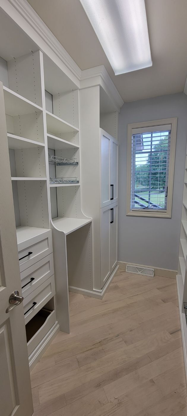 a walk in closet with lots of shelves and drawers and a window .