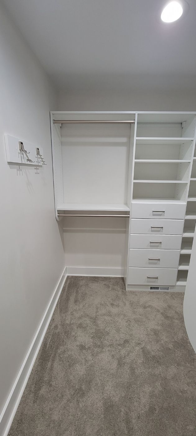 a walk in closet with white shelves and drawers and a carpeted floor .