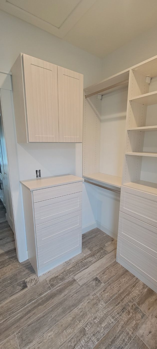 a walk in closet with white cabinets , shelves , and a desk .