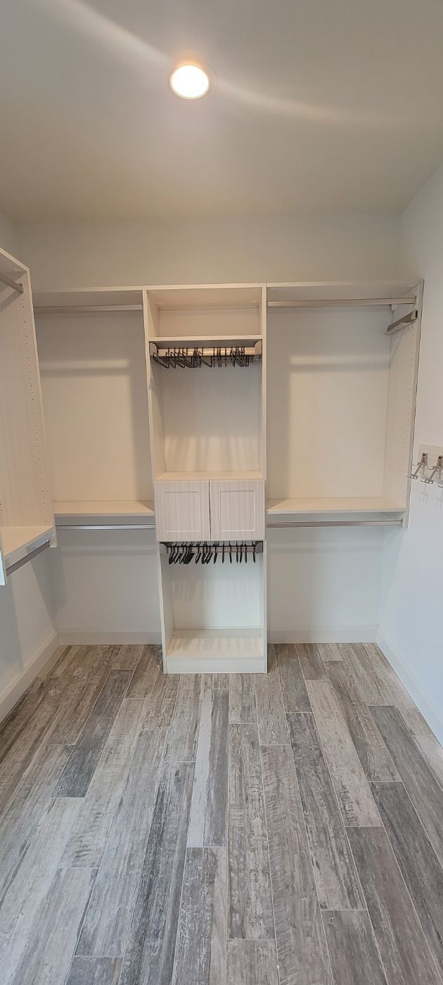 a walk in closet with lots of shelves and a wooden floor .