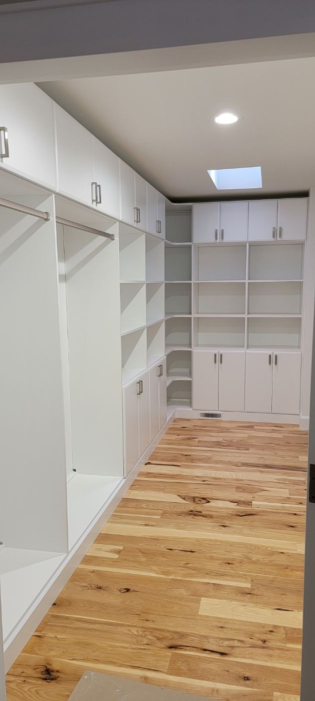 a walk in closet with wooden floors and white cabinets .