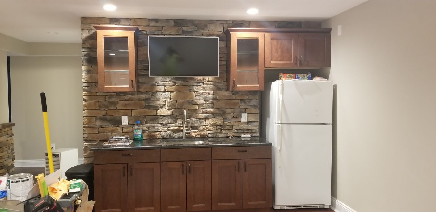 a kitchen with wooden cabinets , a refrigerator , a television and a stone wall .