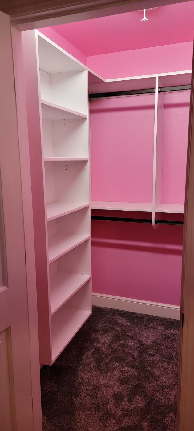 a walk in closet with pink walls and white shelves .