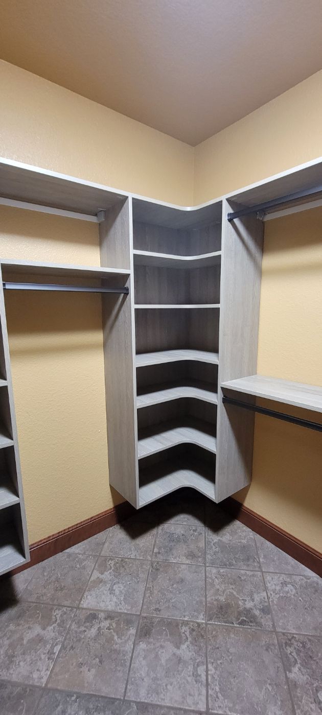 a walk in closet with lots of shelves and hanging clothes .