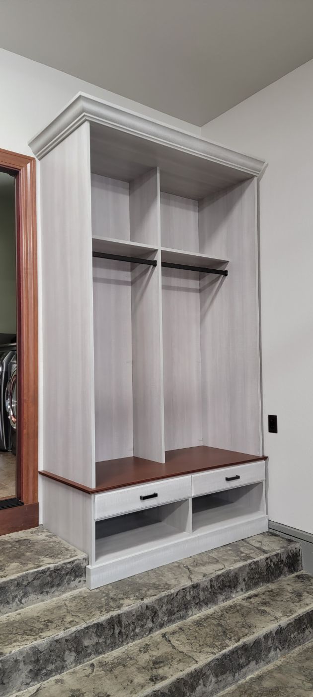 a white closet with wooden shelves and drawers in a room with stairs .