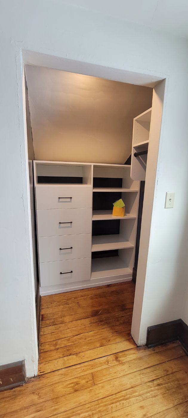 a walk in closet with a wooden floor and white drawers and shelves .