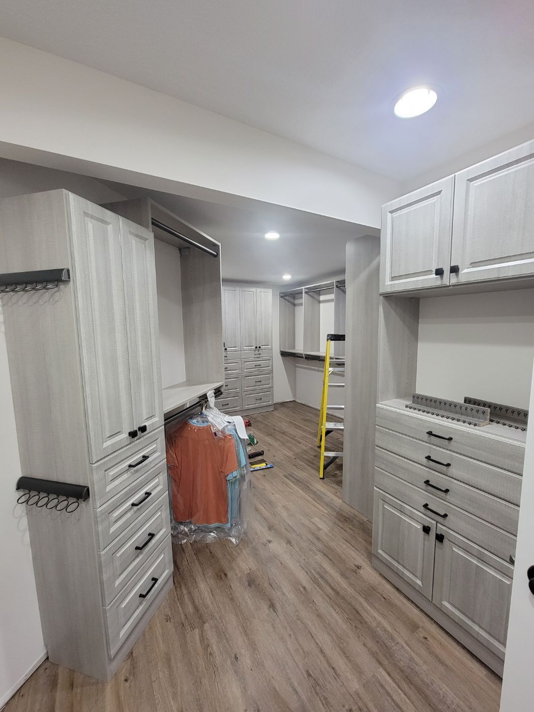 a walk in closet with lots of cabinets and drawers and a yellow ladder .