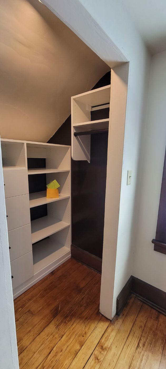 a closet with wooden floors and shelves in a room with a window .