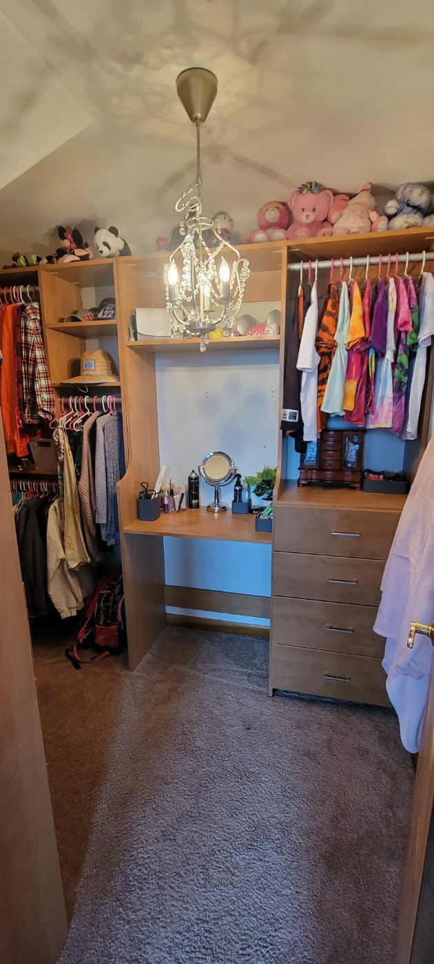 a walk in closet with a desk , dresser , and chandelier .