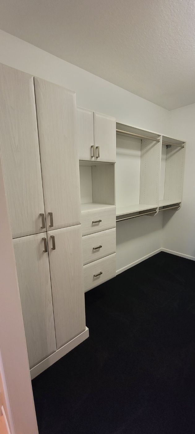 a walk in closet with white cabinets and drawers and a black carpet .