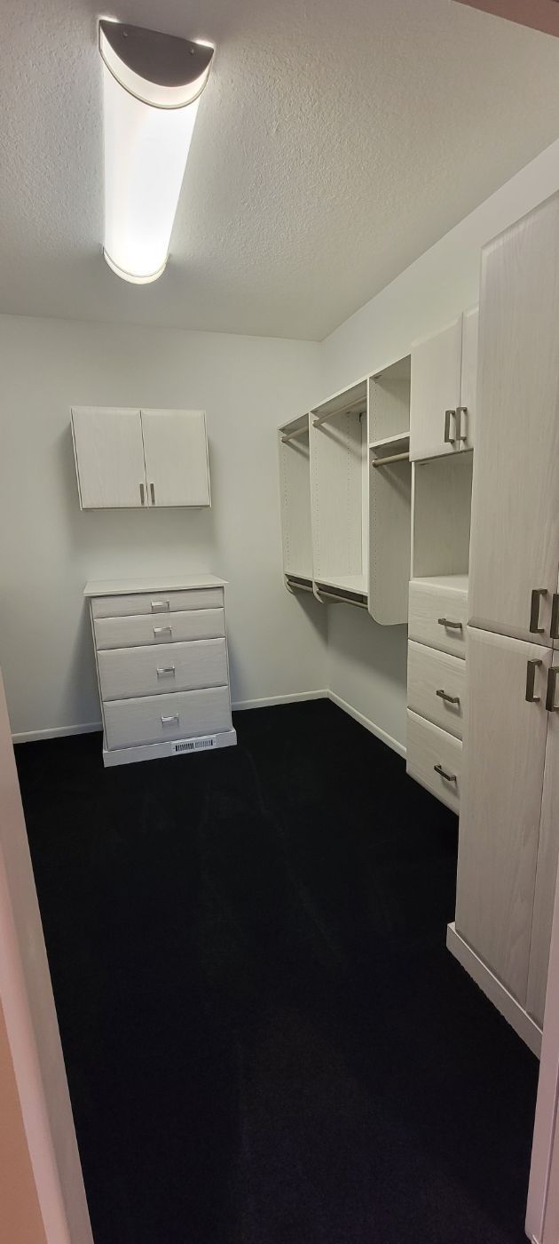 a walk in closet with white cabinets and black carpet .