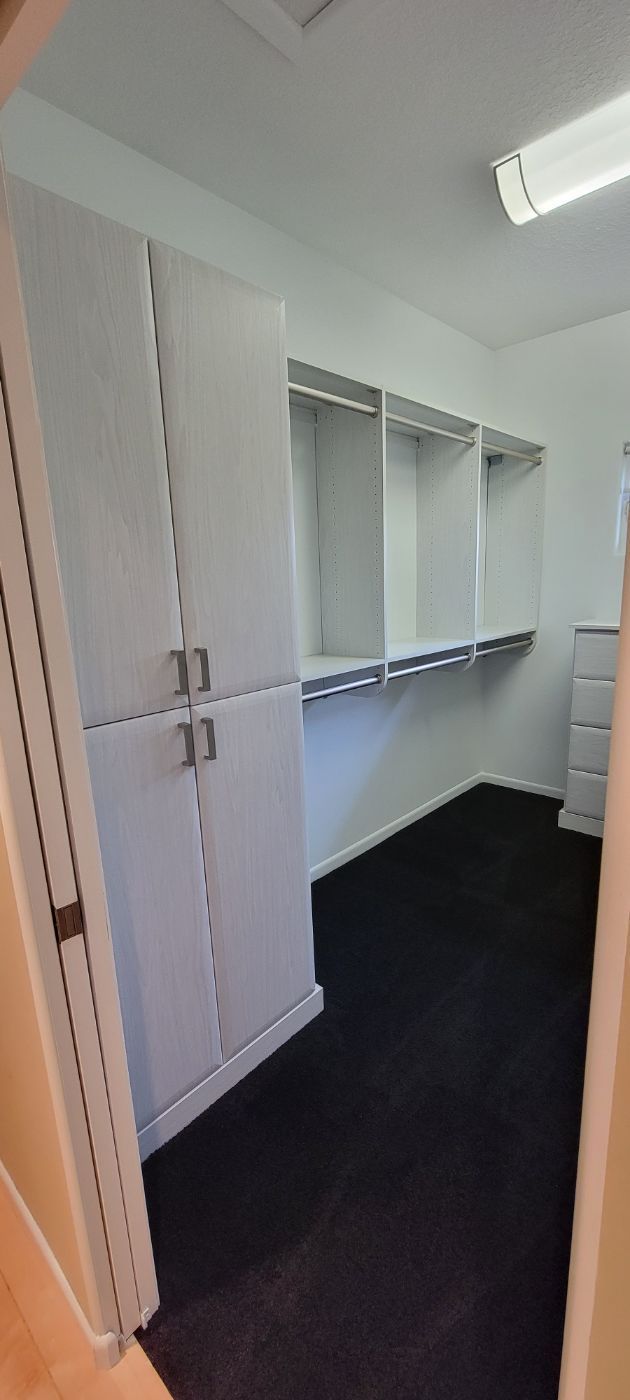 a walk in closet with white cabinets and black carpet .