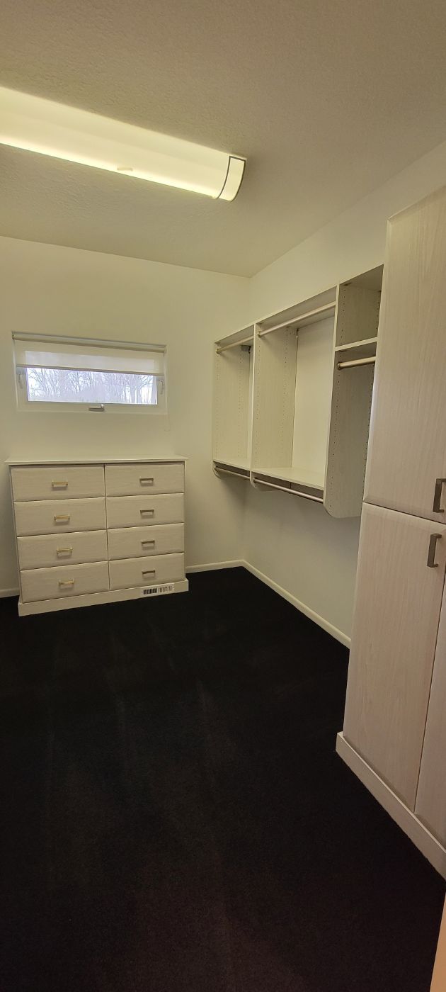 an empty walk in closet with a dresser and a window .