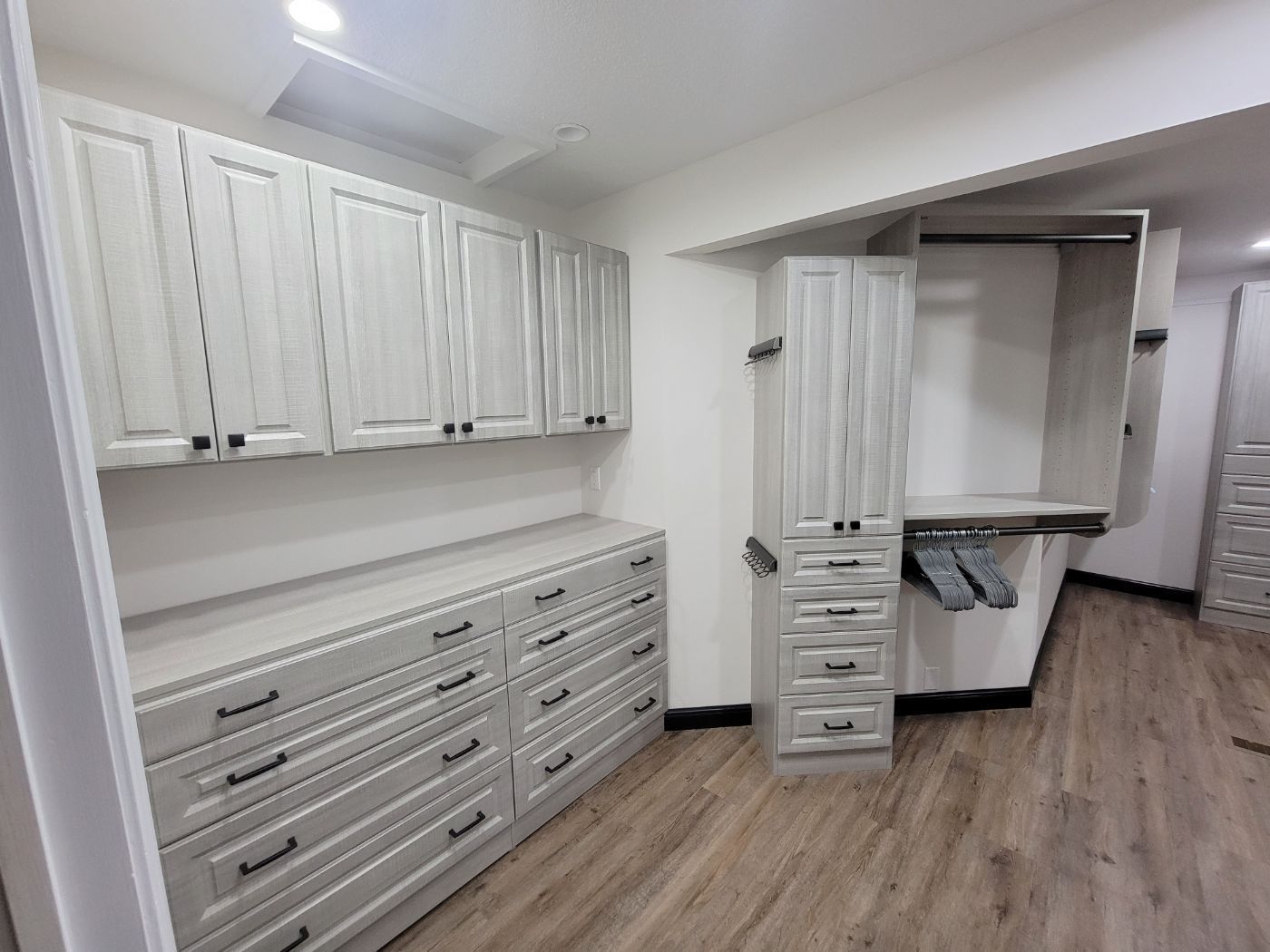 a walk in closet with white cabinets and wooden floors .
