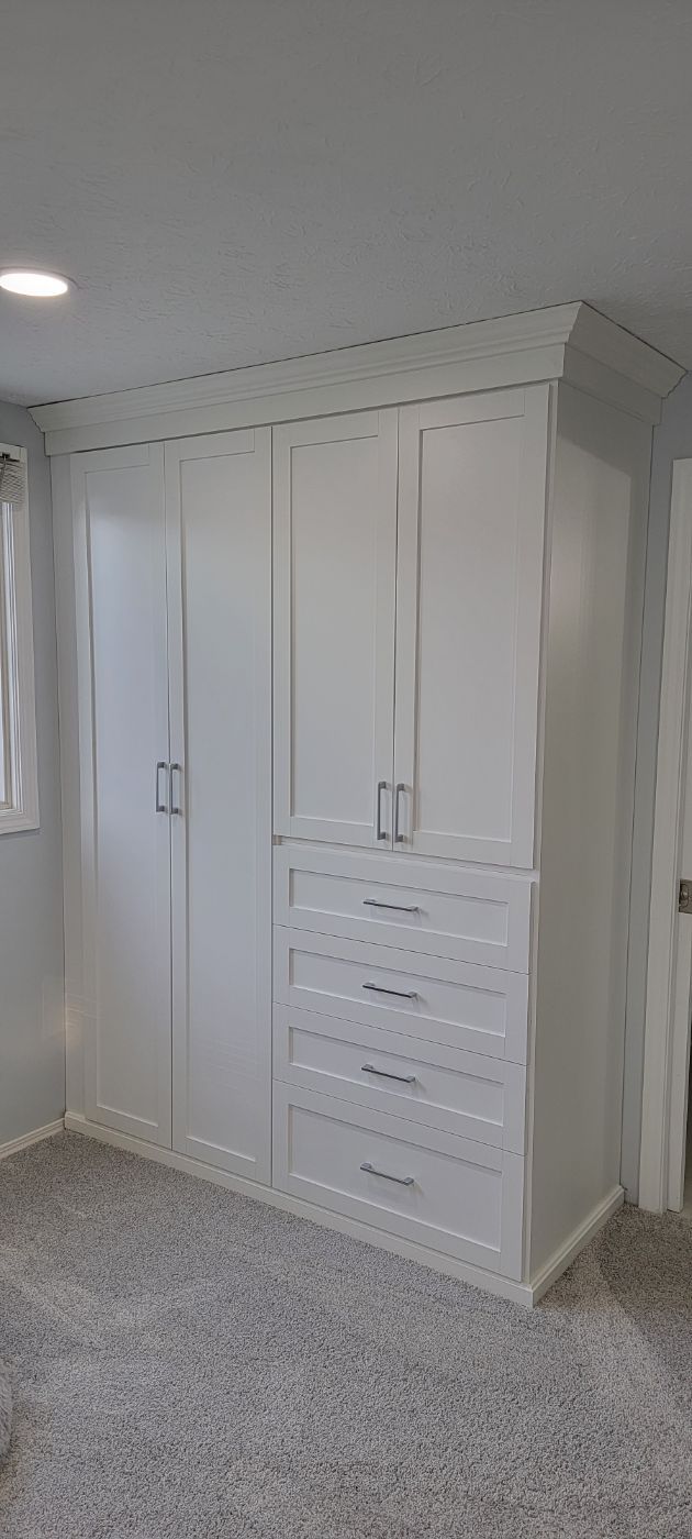 a bedroom with white cabinets and drawers and a window .