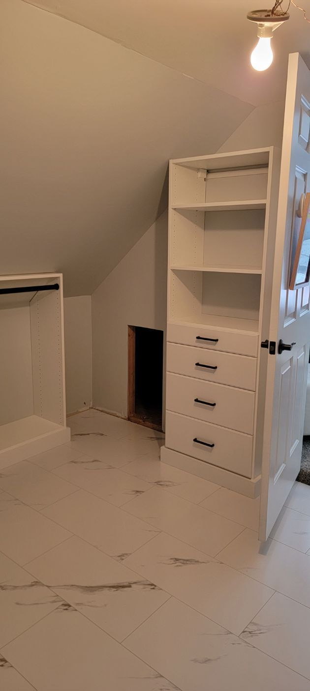 a walk in closet with a slanted ceiling and white shelves and drawers .