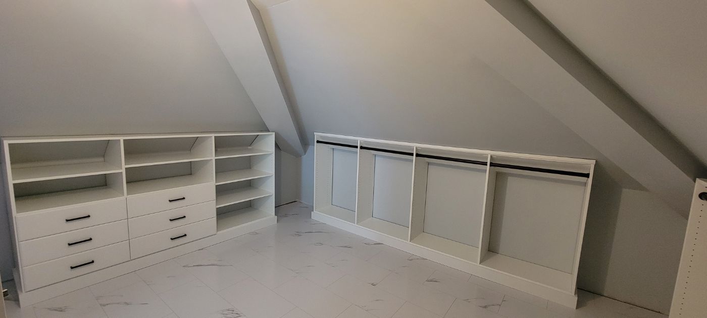 a walk in closet in an attic with lots of shelves and drawers .