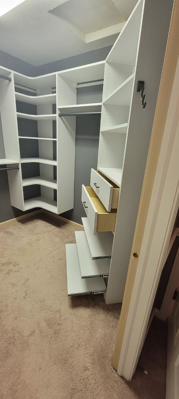 a walk in closet with white shelves and drawers and a door open .