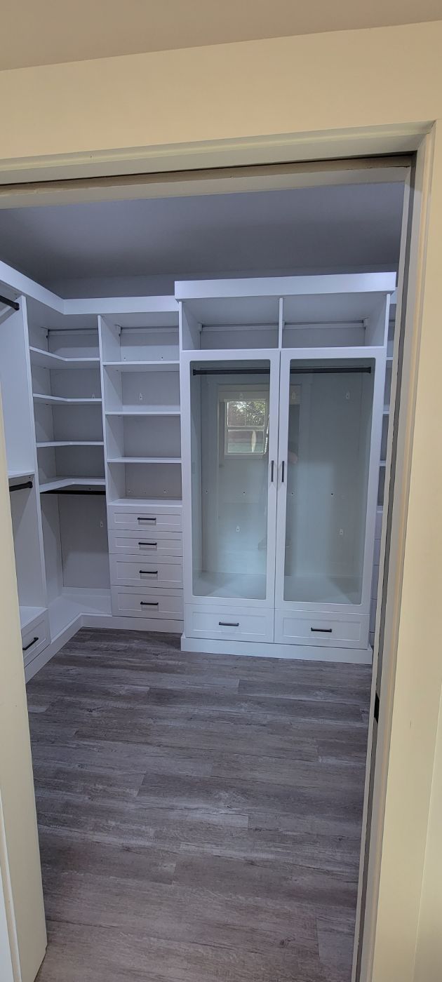 a walk in closet with lots of shelves and drawers and a wooden floor .