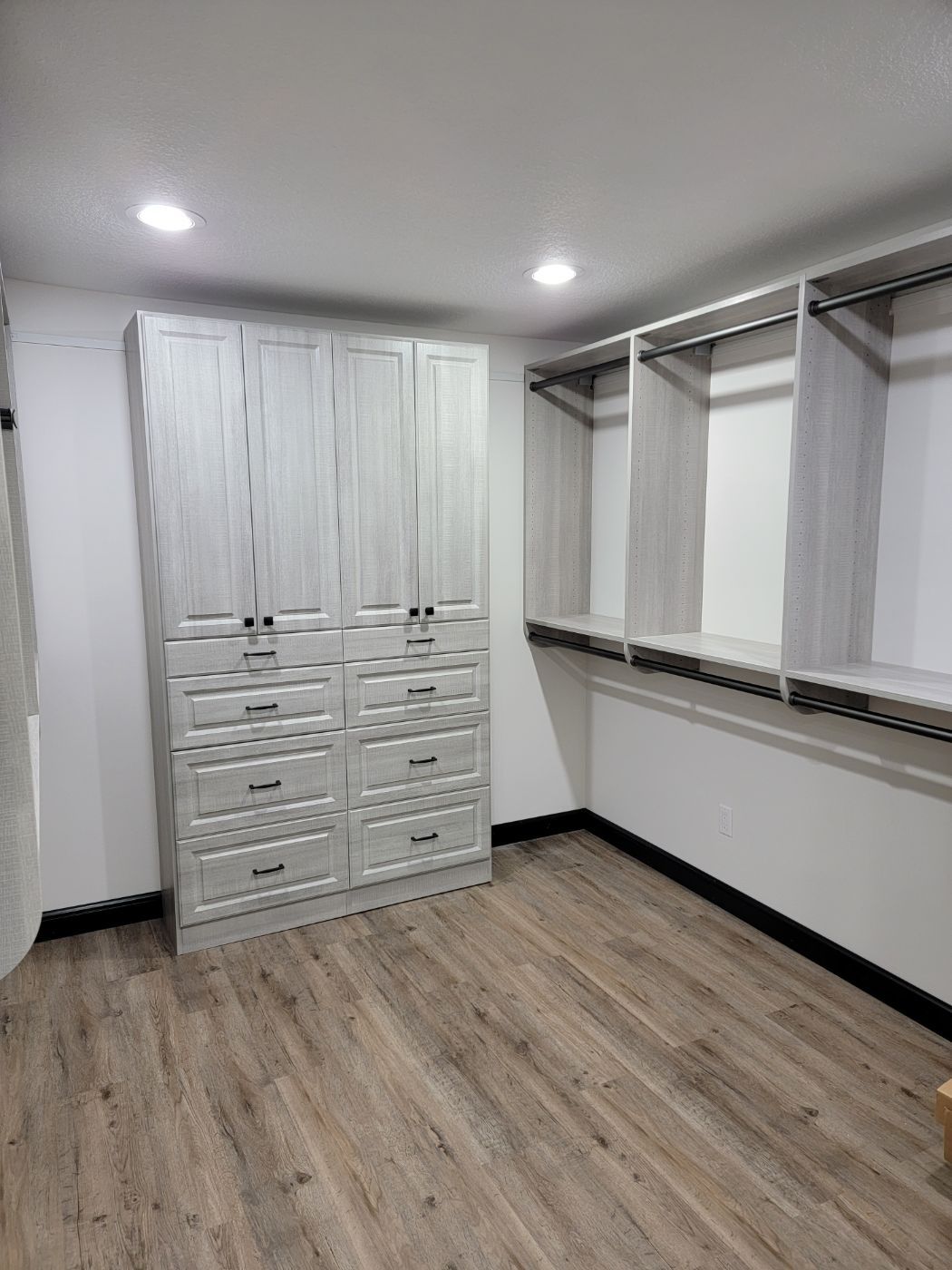 a walk in closet with white cabinets and wooden floors .