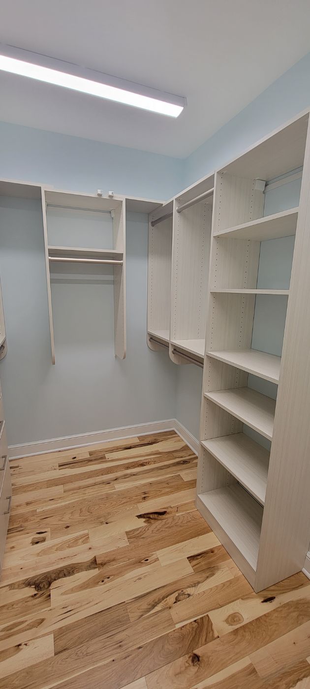 a walk in closet with hardwood floors and white shelves .