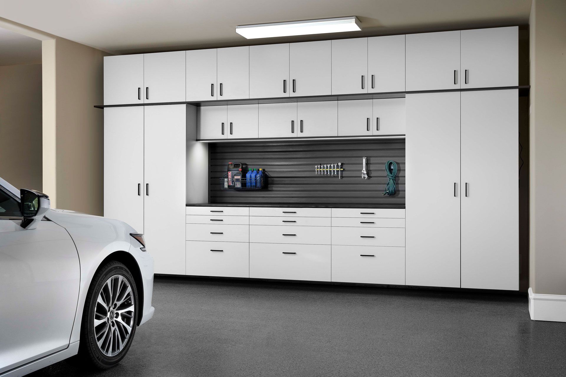White garage with car. Cabinets, drawers, and tools.
