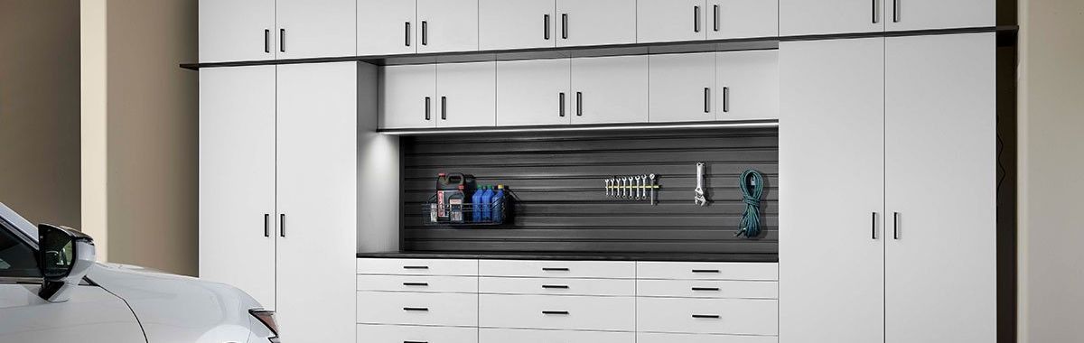 A car is parked in a garage next to a wall of white cabinets.