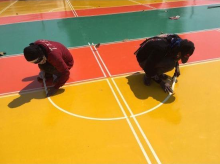Workers kneeling to paint detailed white court lines on a colorful surface during a court installation service in San Tan Valley, AZ
