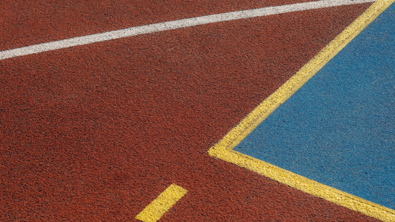 Close-up of red and blue textured court surfacing with yellow boundary lines during a court installation service in San Tan Valley, AZ