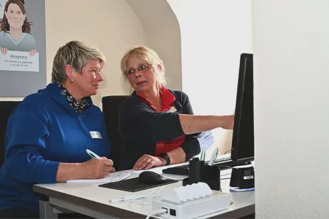 Zwei Frauen sitzen an einem Schreibtisch und schauen auf einen Computerbildschirm.