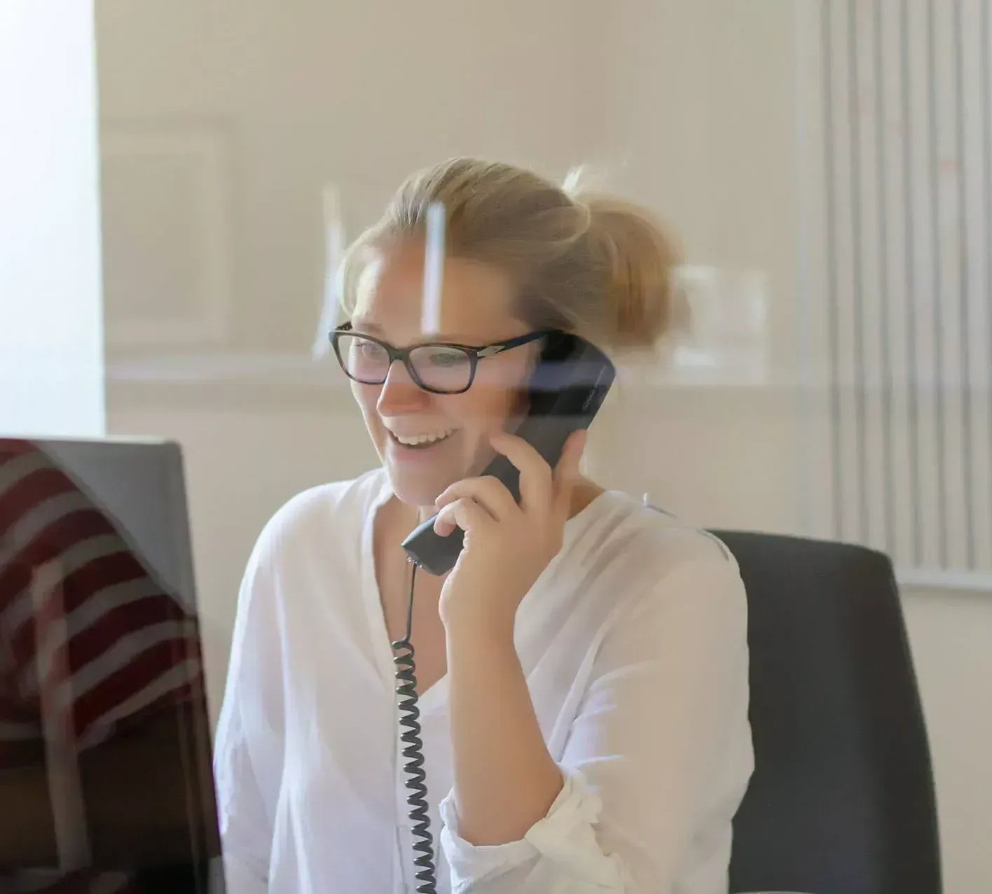 Eine Frau mit Brille lächelt, während sie telefoniert