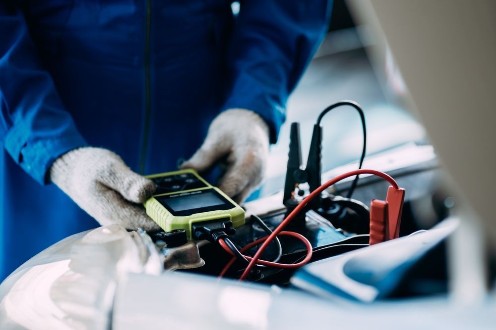 Mechanic in Blue Uniform and Gloves, Testing Car Battery — A1 Mobile Safety Certificates in Edge Hill, QLD