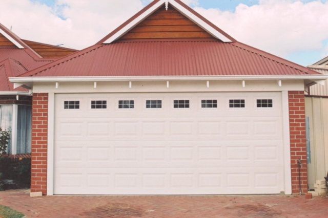 A white garage door is in front of a house with a red roof