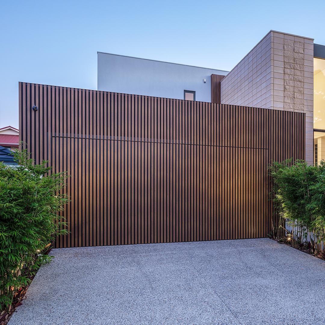 A large wooden fence is surrounding a gravel driveway in front of a house.