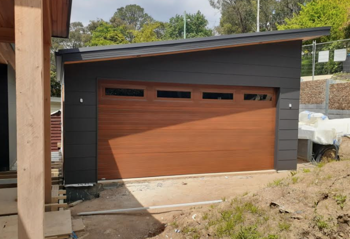 A garage with a wooden door is being built next to a house.