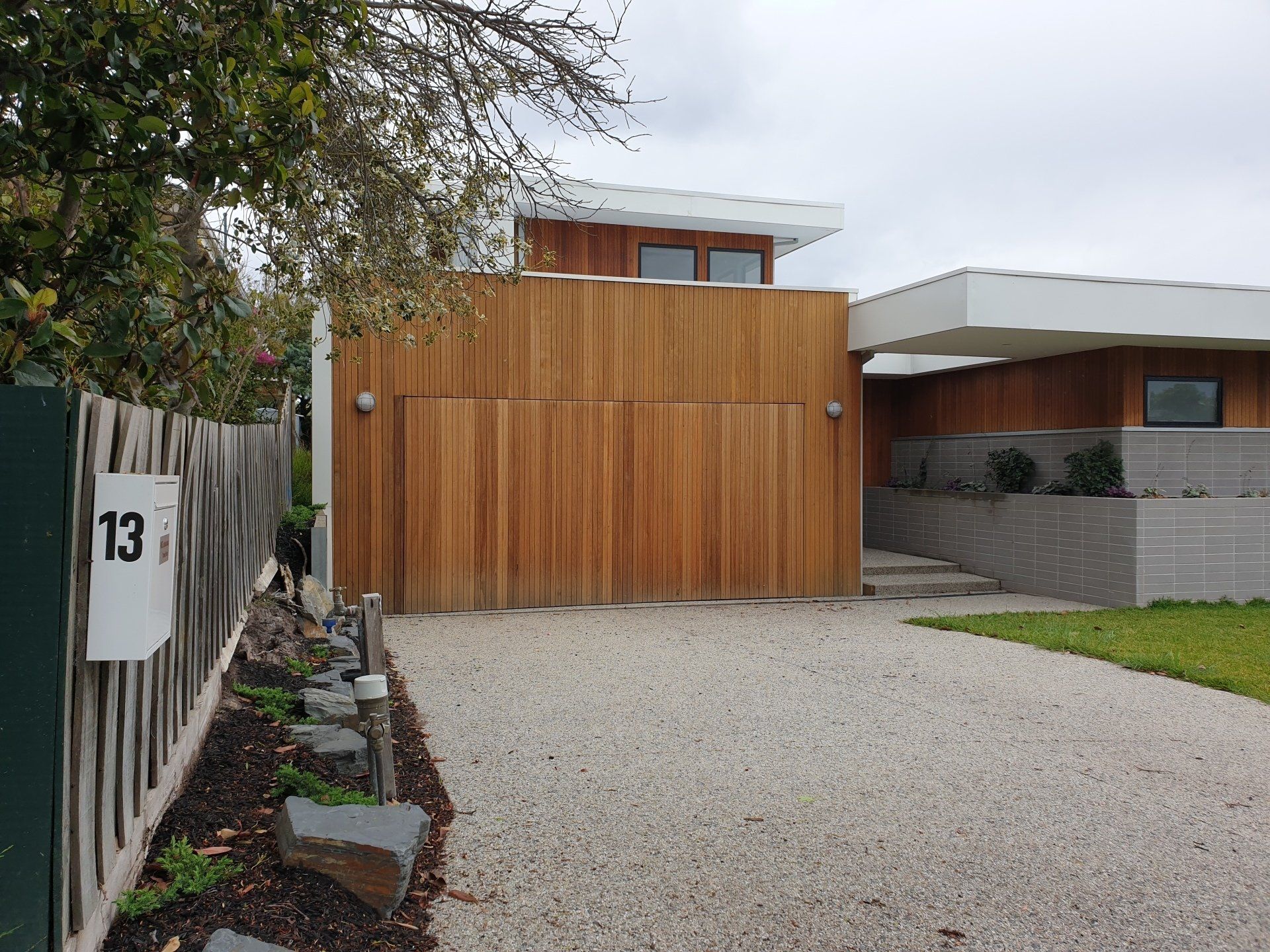 A house with a wooden garage door and a gravel driveway leading to it.