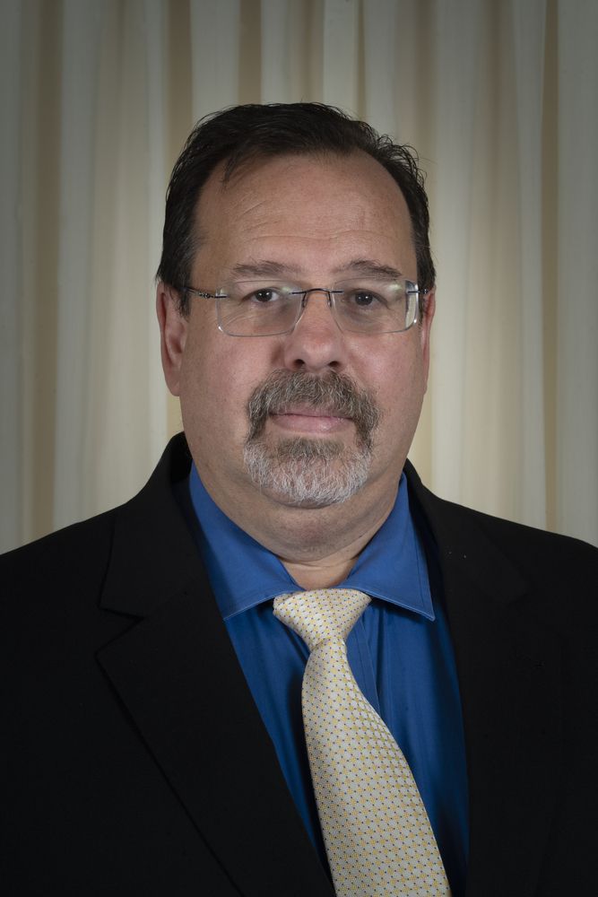 A man with a beard and glasses is wearing a suit and tie.